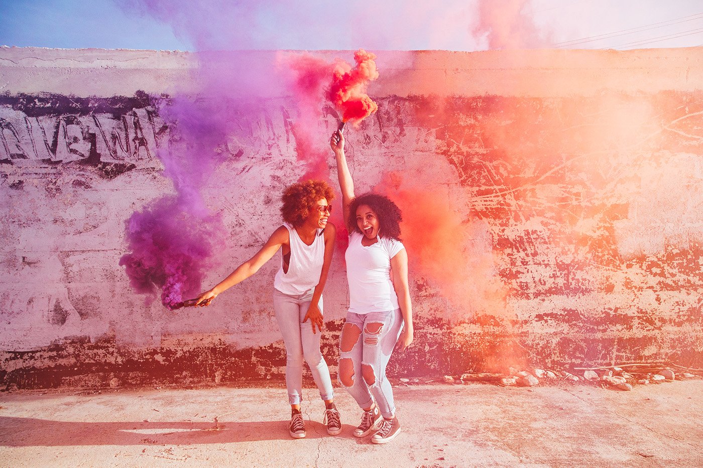 Two woman playing with smoke bomb in front of a painted wall.