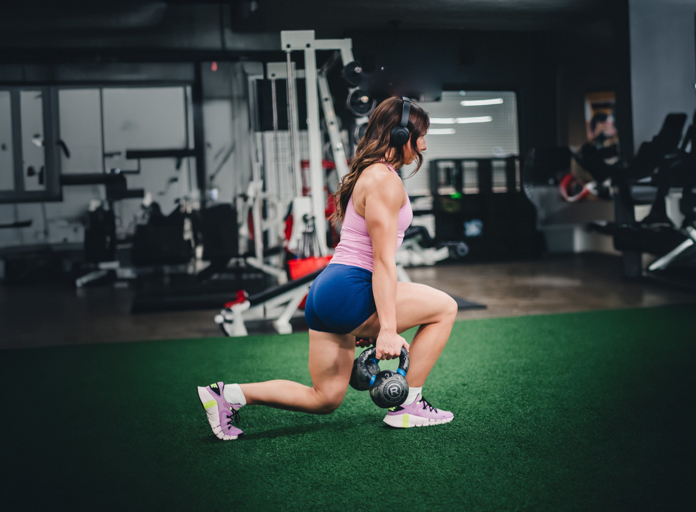 Woman at gym holds weights while lunging and wearing black wicked audio headphones