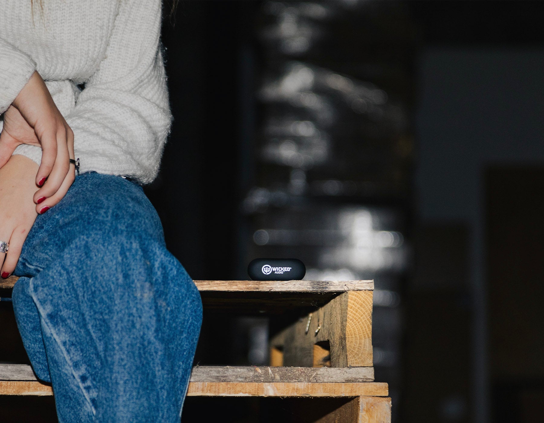 earbuds in case sit next to woman in jeans