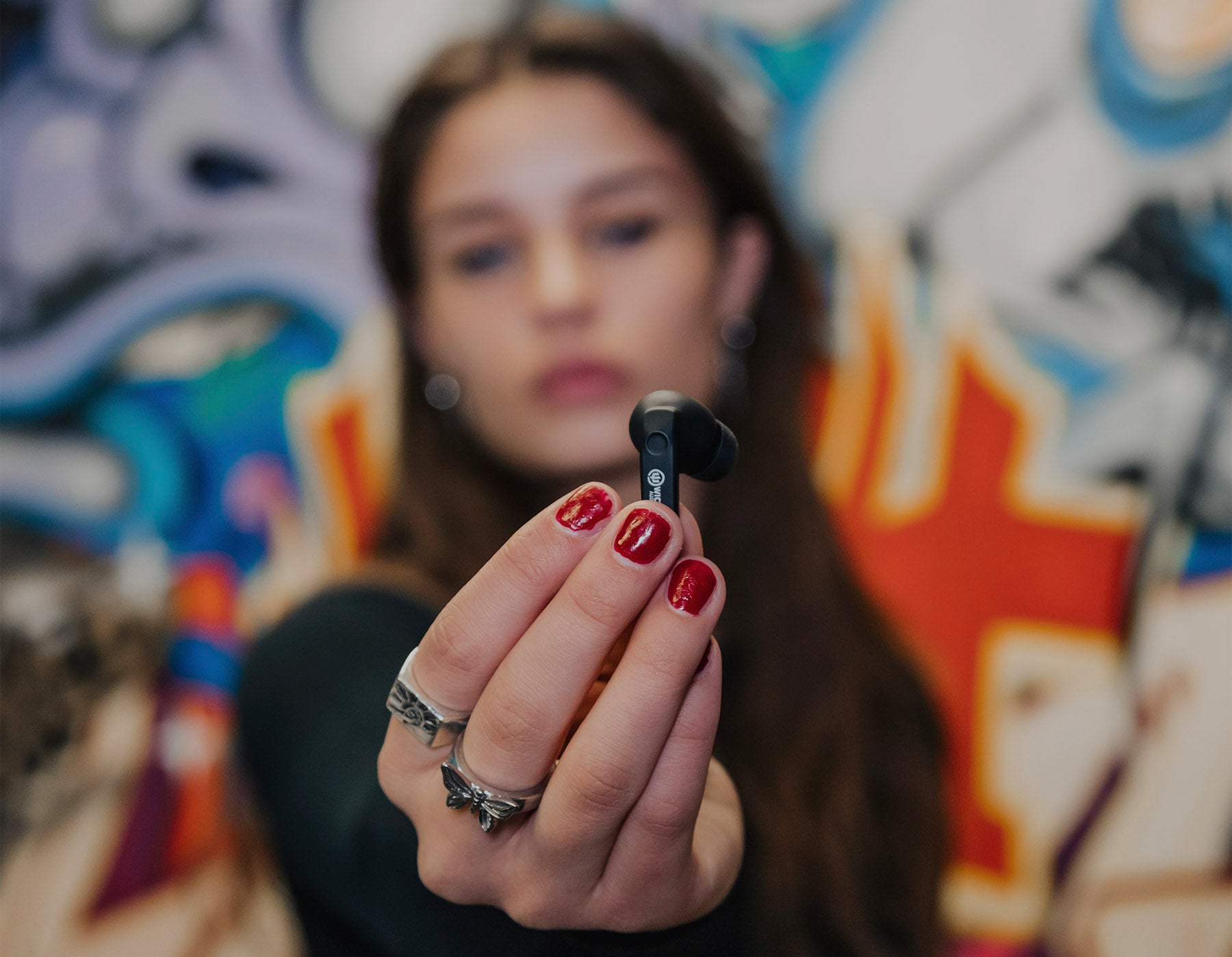 Woman with red nail polish holds earbud towards camera