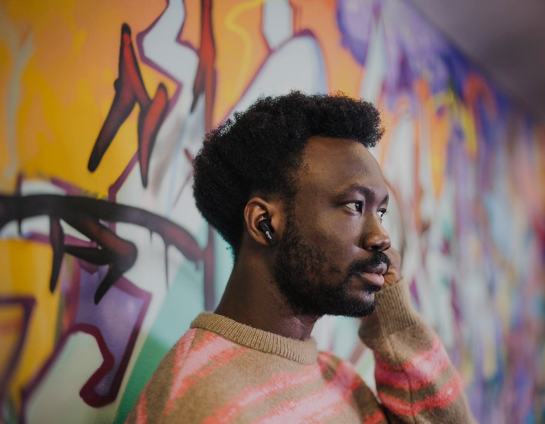 Man against graffiti wall adjusts earbud