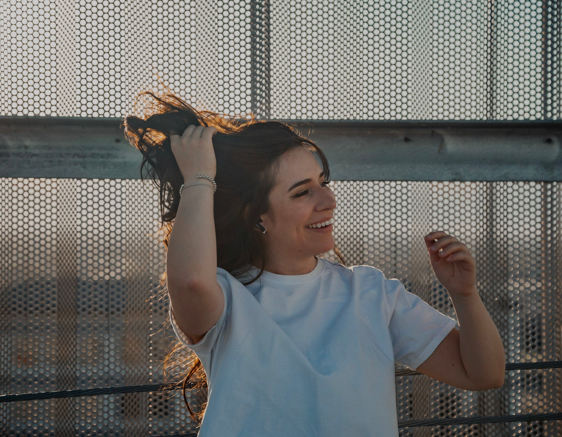 Woman laughs while adjusting her hair and wearing earbuds