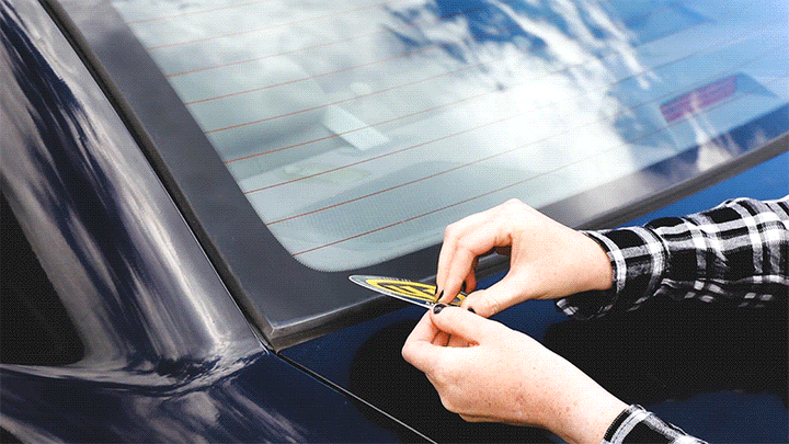 Sticker being unpeeled and placed on the back windshield of a car