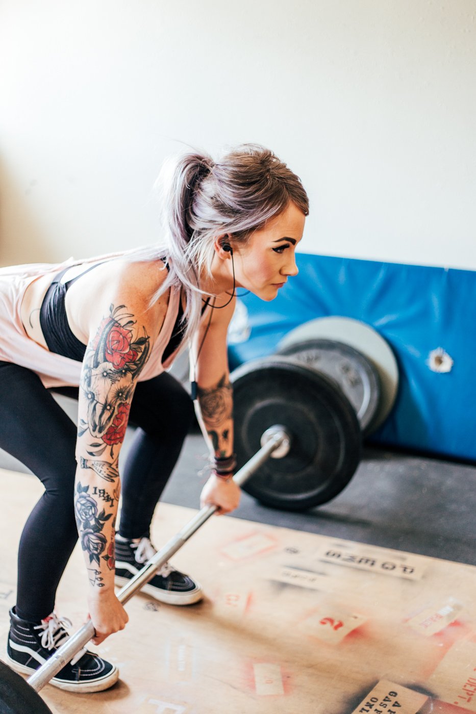 Tattooed woman weightlifting while wearing earbuds.
