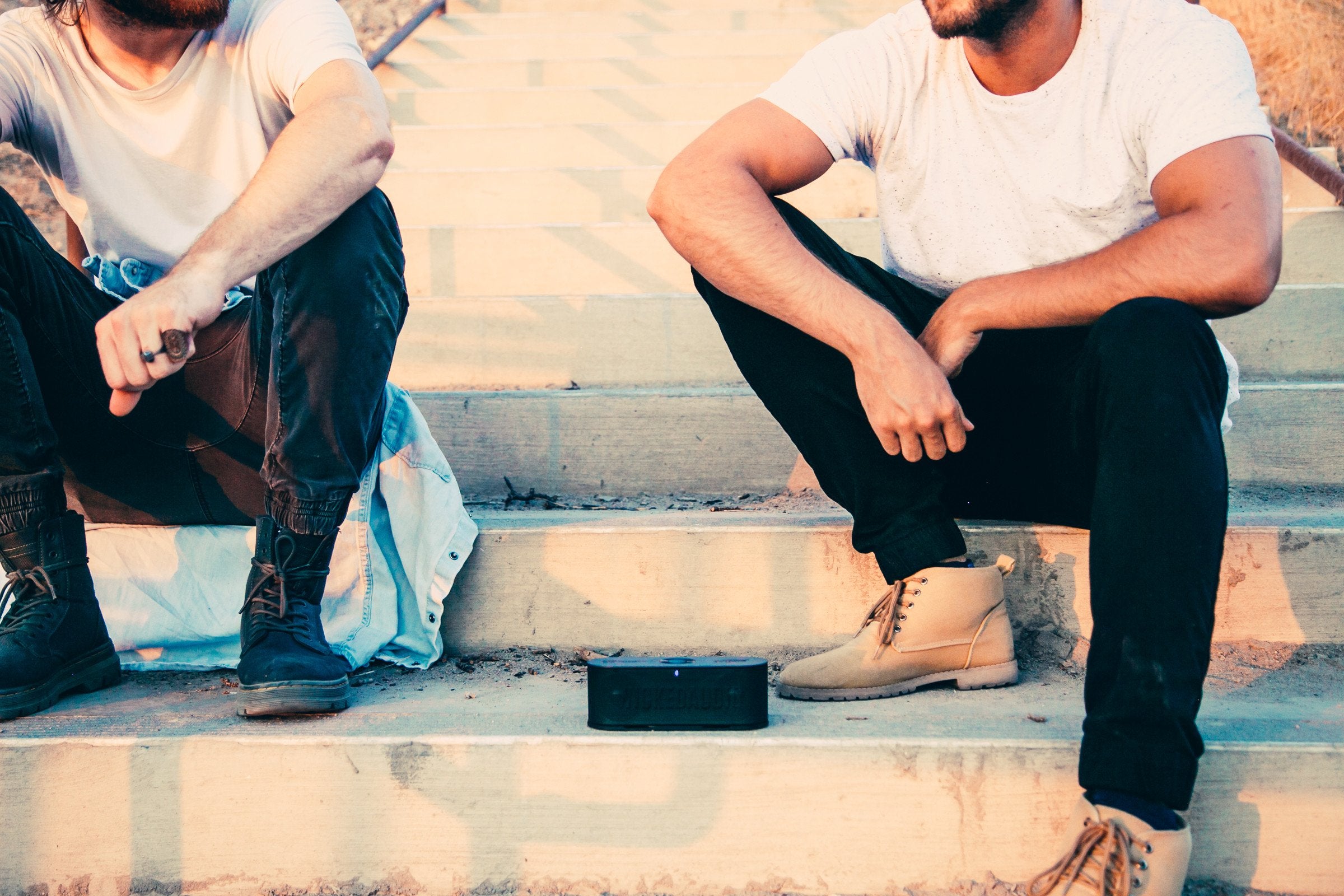 Shot of men sitting on stairs with bluetooth speaker between them.