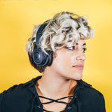 Model on yellow background wearing Endo Wireless Headphone. She is looking off to the side and has short curly hair.